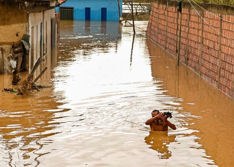 Un hombre carga a su perro en una calle inundada en Itapetinga, estado de Bahia, Brasil, el lunes 27 de diciembre de 2021. (AP Foto/Manuella Luana)