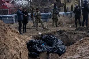 FILE - People standing next to a mass grave in Bucha, on the outskirts of Kyiv, Ukraine, on April 4, 2022. AP reporters saw dozens of bodies in the streets of Bucha, many of them shot at close range and some with hands tied behind the back.  .  (Photo AP / Rodrigo Abd)