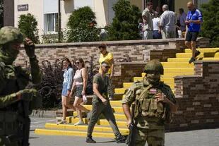 People walk past as Russian soldiers guard a Russian citizenship application office in Melitopol, southern Ukraine, on July 14, 2022.