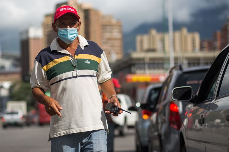 Un trabajador de una gasolinera ayuda a organizar la fila de autos que esperan para llenar sus tanques afuera de una gasolinera en Caracas el 5 de octubre de 2020
