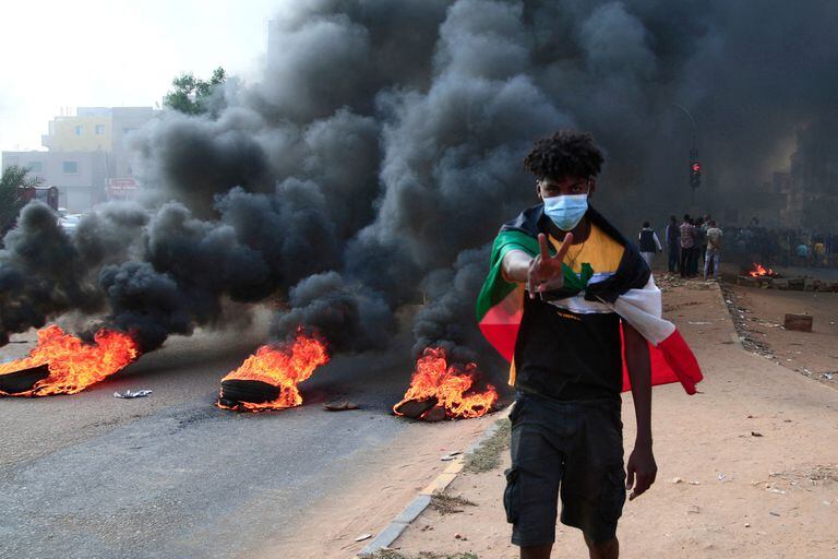 Un manifestante sudanés envuelto con la bandera nacional muestra el signo de la victoria junto a neumáticos en llamas durante una manifestación en la capital para denunciar las detenciones nocturnas por parte del ejército de miembros del gobierno de Sudán