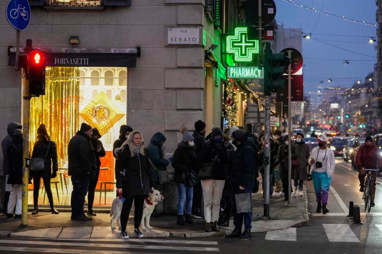 Numerosas personas hacen fila afuera de una farmacia donde se efectuan pruebas diagnósticas de COVID-19, el jueves 23 de diciembre de 2021, frente a la catedral de Milán, Italia. (AP Foto/Luca Bruno)