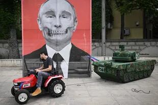 Un activista pasa con un tractor frente a un retrato del presidente ruso Vladimir Putin en una burla contra el mandatario frente a la embajada rusa en Bucarest 