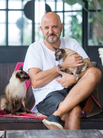 Diseñada por el arquitecto Alejandro Goldstein, con quien trabajó codo a codo, tanto la arquitectura como el interiorismo son de espíritu ecléctico. En la foto, posa con Lucca y Elsa, sus gatos siameses, en la galería.