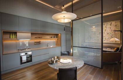 El comedor con cocina integrada (Arquimadera). La mesa circular (Hábito) con tapa travertino silver (Canteras del mundo) está acompañada por sillas Trabadas de vaqueta (Azcue). Sobre ellas, lámpara colgante Flamingo (Iluminación Agüero). Las paredes están recubiertas con papel textil Vescom.