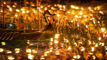Los miembros vestidos con trajes vikingos llevan antorchas encendidas antes de quemar la galera
