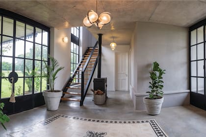 El hall de entrada cuenta con dos grandes puertas de hierro y vidrio repartido, que fueron hechas a medida. Una lámpara original de los años 60 organiza el espacio, junto con el cuadrante de piso calcáreo, con una flor de lis central.