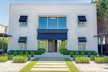 Simetría perfecta en la fachada, donde el blanco impecable se corta con los toldos y las macetas negras.