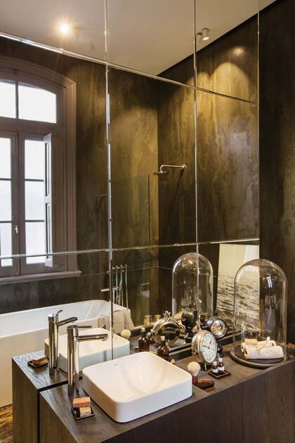 El sector de lavado de manos, con mueble revestido en madera y bacha semiembutida, con relojes antiguos y adornos (Baardo y Landmark). El piso, de porcelanato, a esa altura está recubierto con una pieza de piedra natural de cantera que da un original efecto alfombra.