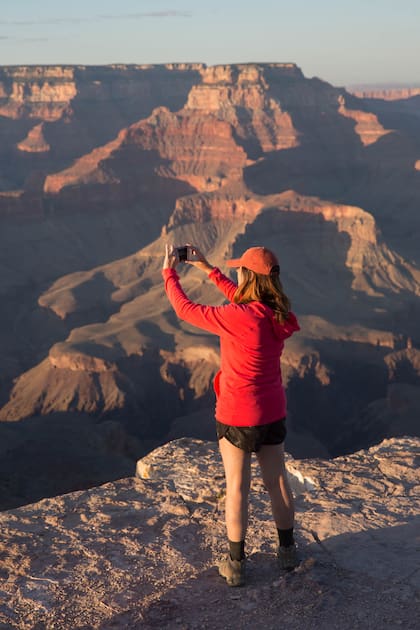 Una turista intenta capturar la imponencia del paisaje del Gran Cañón al atardecer con su celular.