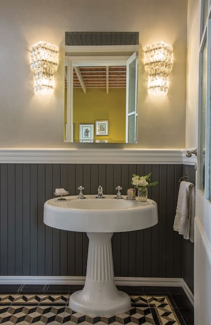 Un detalle del baño principal, donde resaltan dos apliques originales de los 50. El lavatorio de pie es de demolición y el machimbre y las cenefas están dispuestos a la manera inglesa.