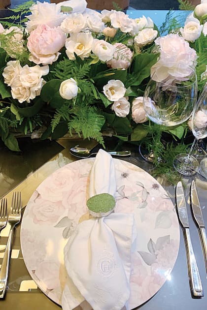 Detalle de un puesto con plato de sitio floreado de la marca Ceci NY, servilleta de Fendi con monograma y anillo de piedra verde