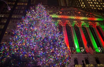 El edificio iluminado de la Bolsa de Nueva York con un gran árbol de Navidad en frente.