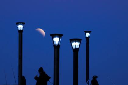 Los hombres se paran debajo de las luces de la calle cuando sale la luna en Buenos Aires, Argentina