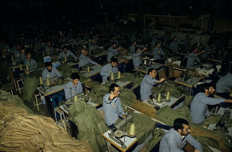 Presos políticos iraníes, con los puños en alto, corean consignas de propaganda en apoyo de la República Islámica, mientras confeccionan ropa, en la prisión de Evin en 1986.