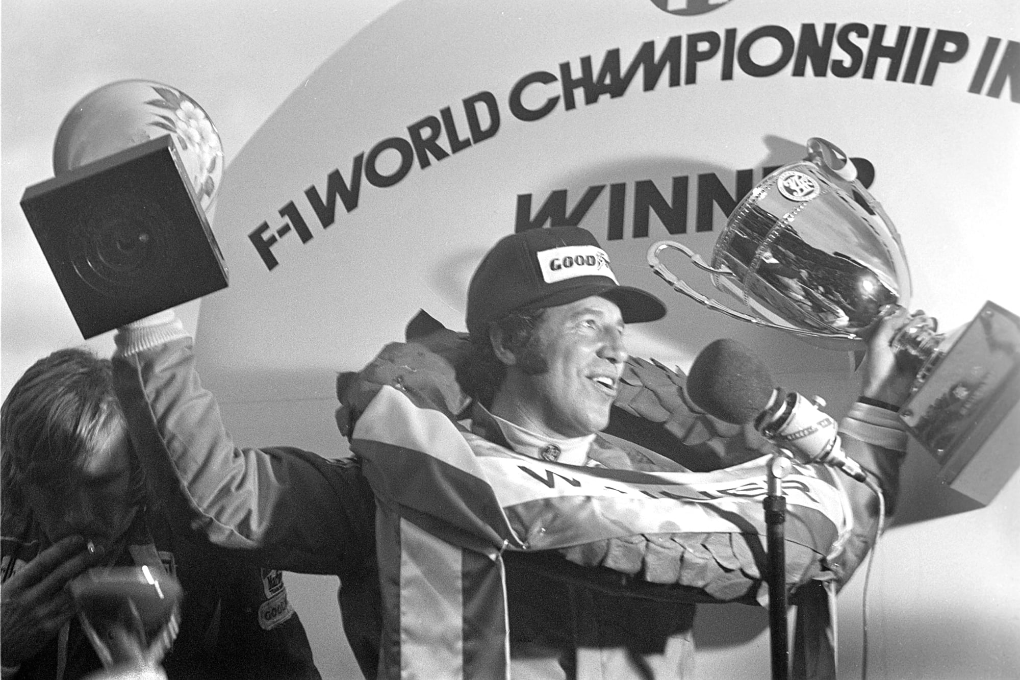Mario Andretti (Lotus) festeja la victoria en el Gran Premio de Japón 1976, mientras James Hunt fuma un cigarrillo en el podio, tras terminar tercero y consagrarse campeón de Fórmula 1
