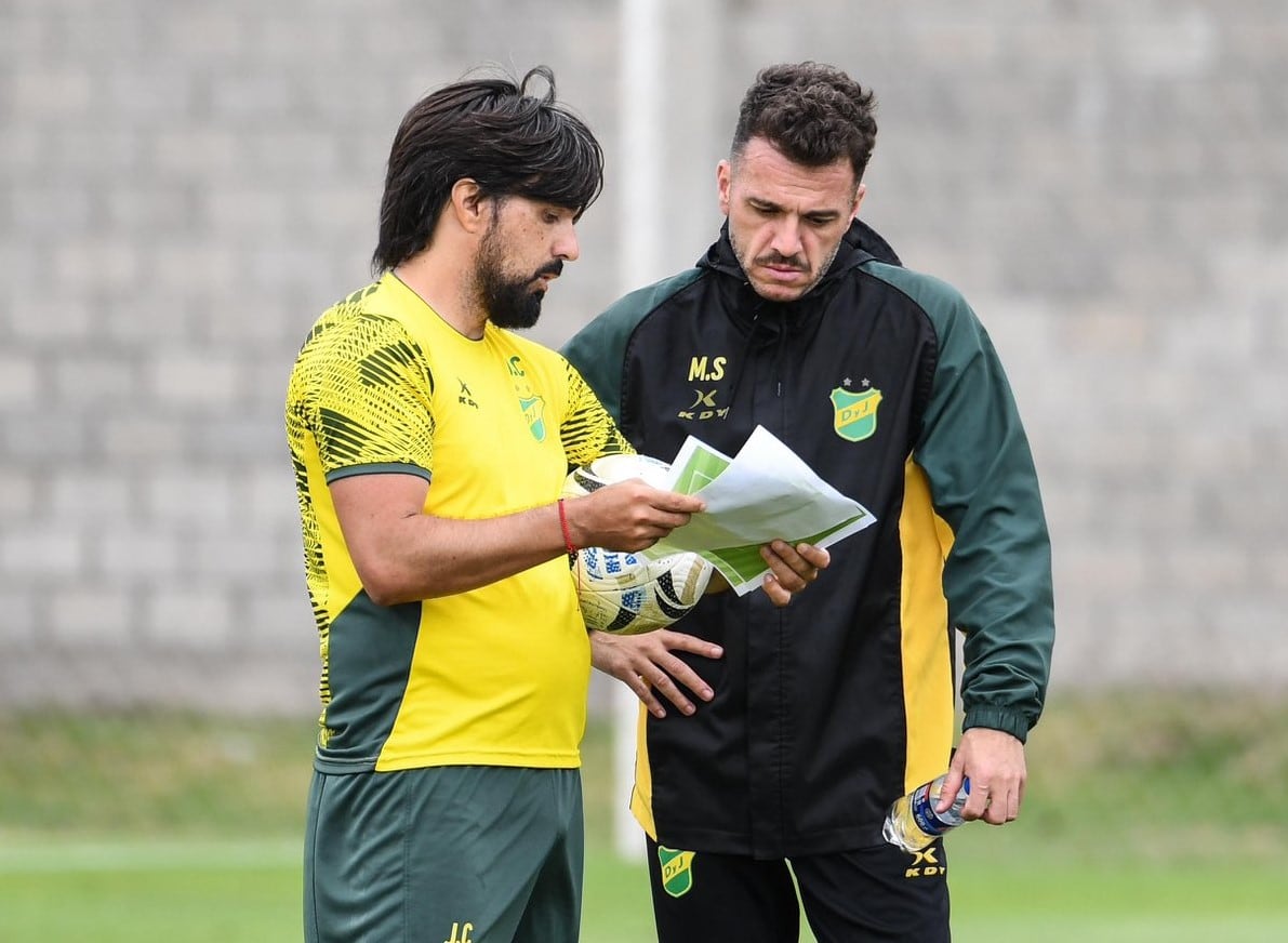 Mariano Soso, DT de Defensa y Justicia, observa papeles que le muestra un colaborador durante un entrenamiento