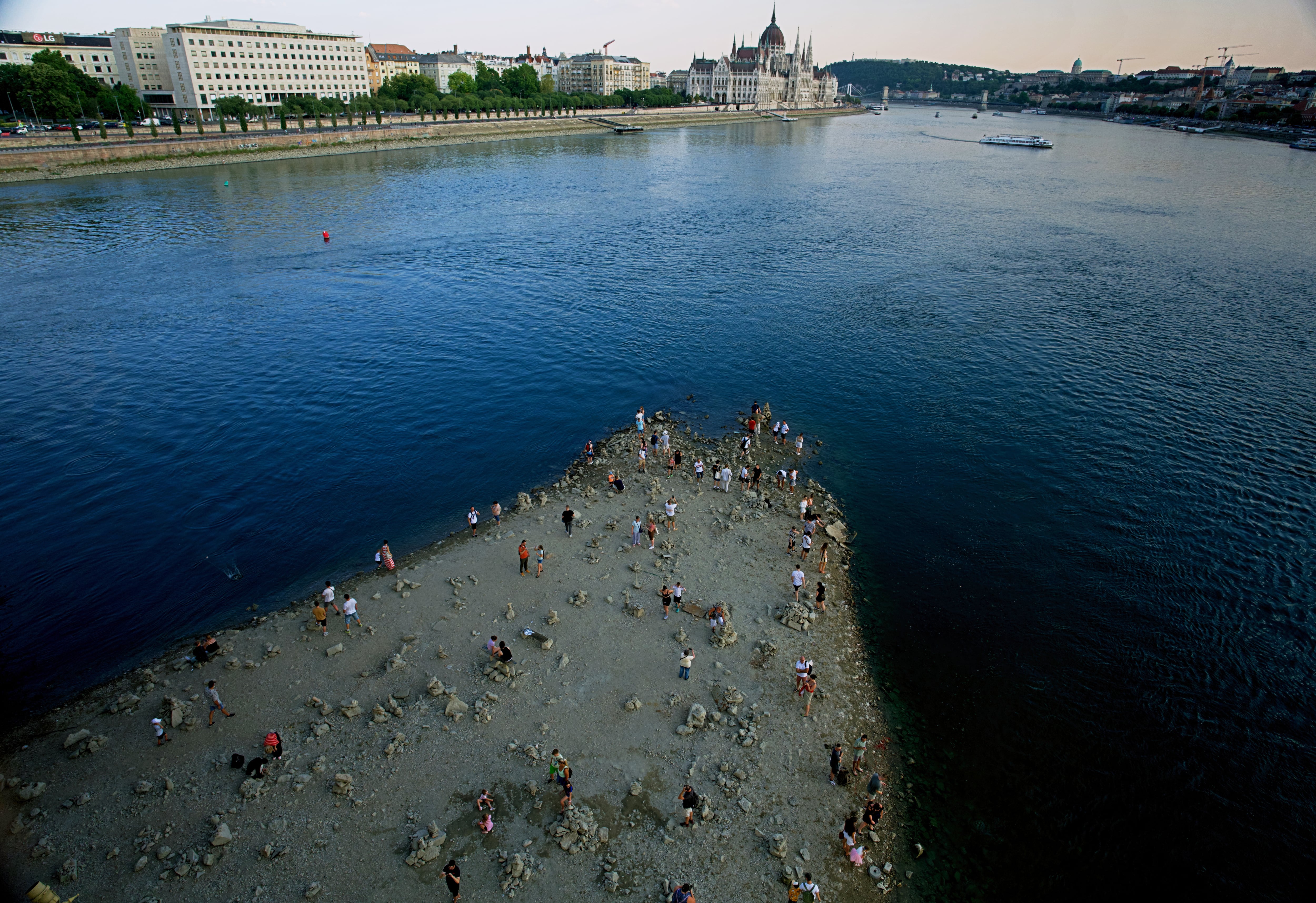 Personas caminan sobre un banco de arena bajo el Puente Margareth del río Danubio, en el centro de Budapest