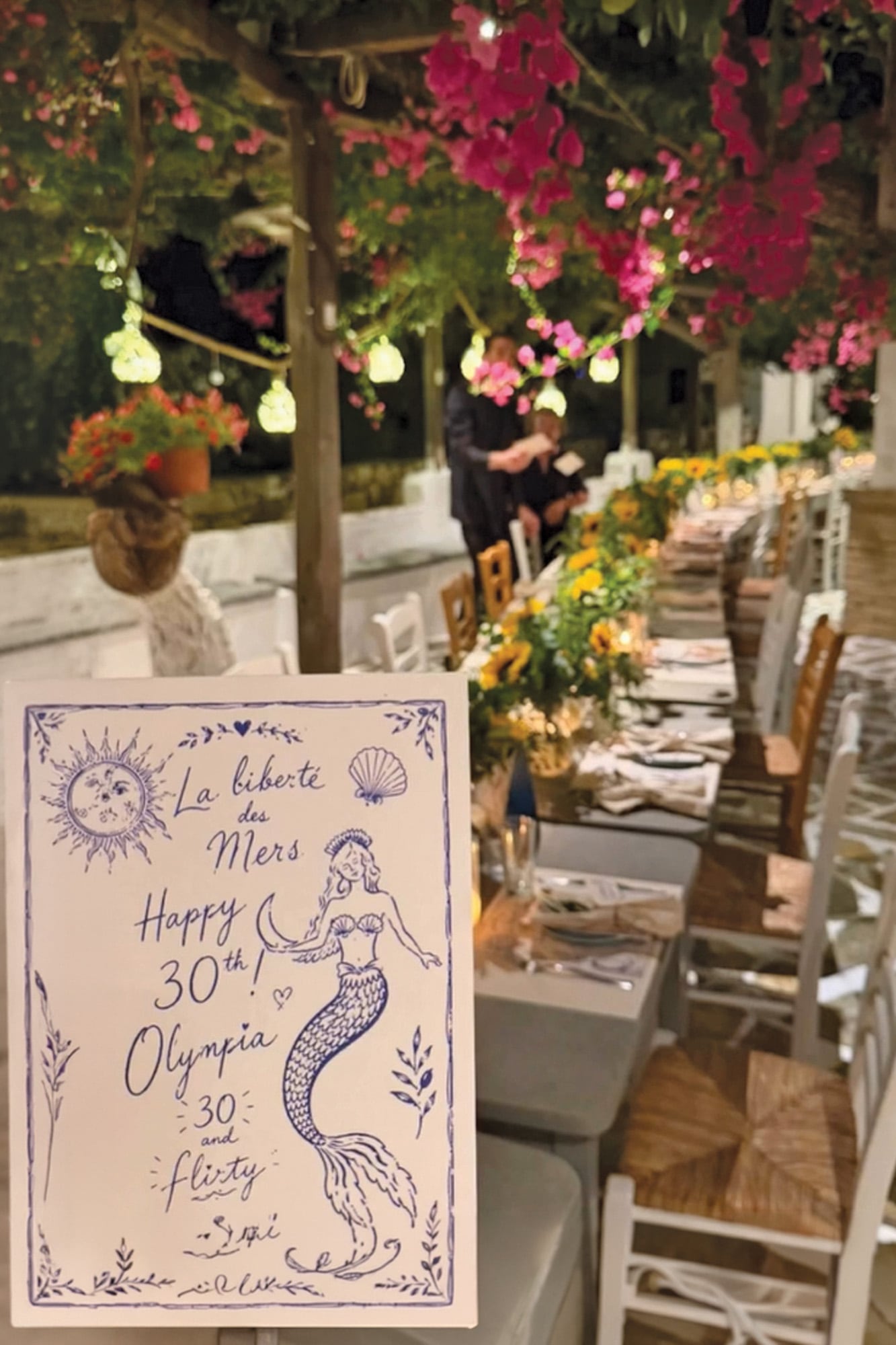 Imagen de la tarjeta de invitación; detrás, la larga mesa de la
Taverna Klimatari decorada con girasoles
