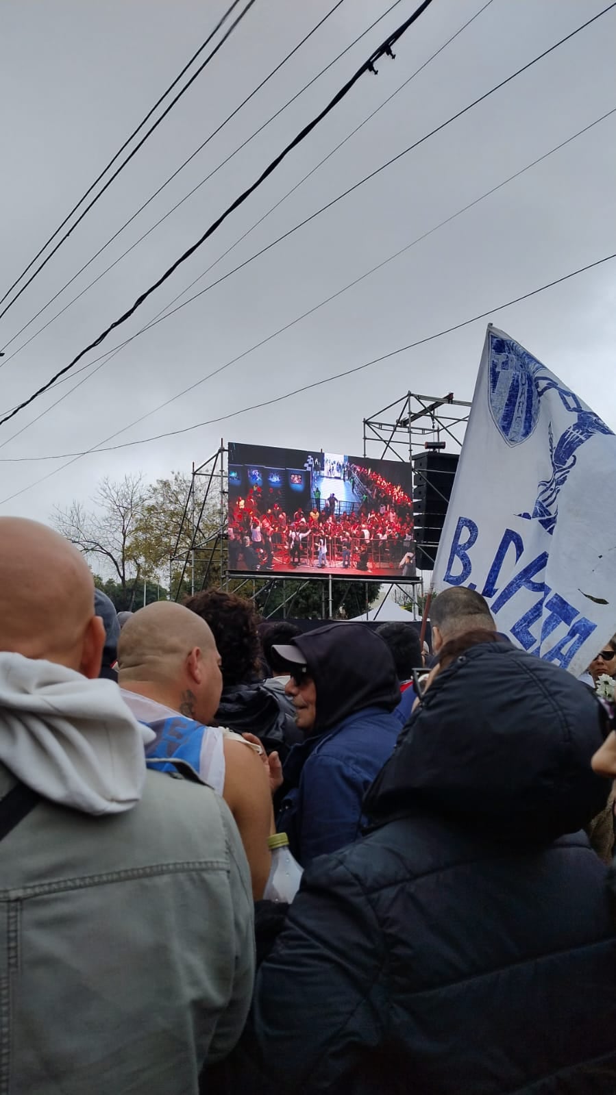Desde la fila se puede observar una pantalla que muestra el interior del Polideportivo Gatica, donde está la Capilla Ardiente