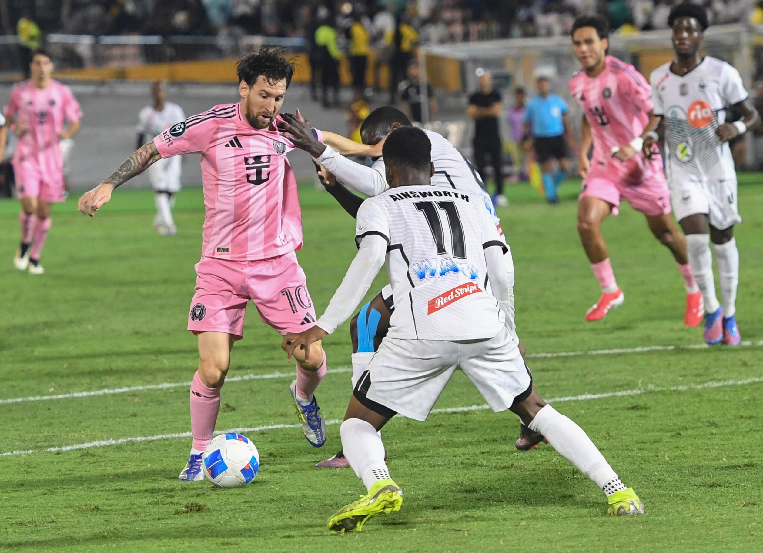El delantero de Inter Miami Lionel Messi, a la izquierda, intenta quitarle el balón a Christopher Ainsworth, del Cavalier de Jamaica, durante un partido de fútbol de la Copa de Campeones de la CONCACAF en Kingston, Jamaica