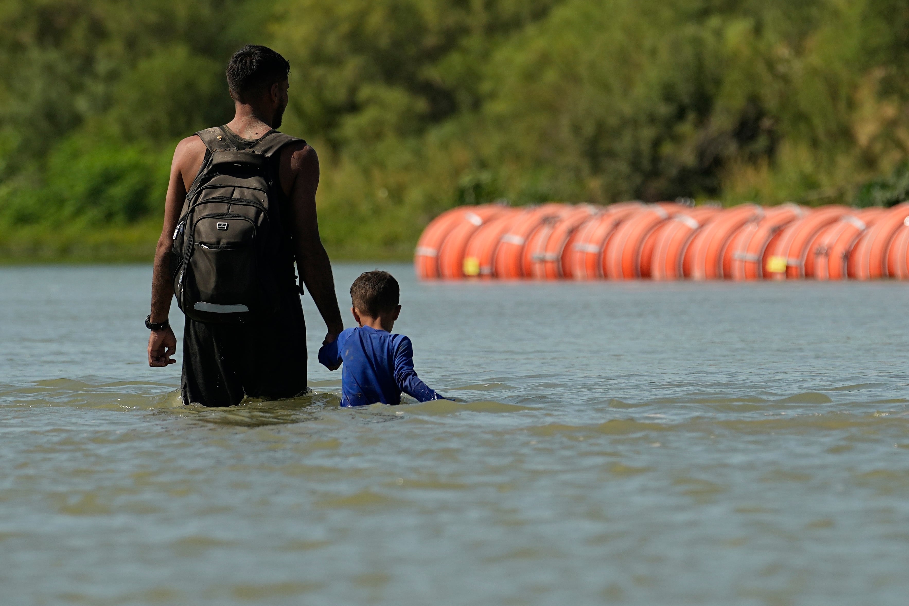 Migrantes caminan hacia unas boyas colocadas por Estados Unidos como una especie de muro flotante en el Río Bravo, en Eagle Pass, Texas. (AP Foto/Eric Gay)