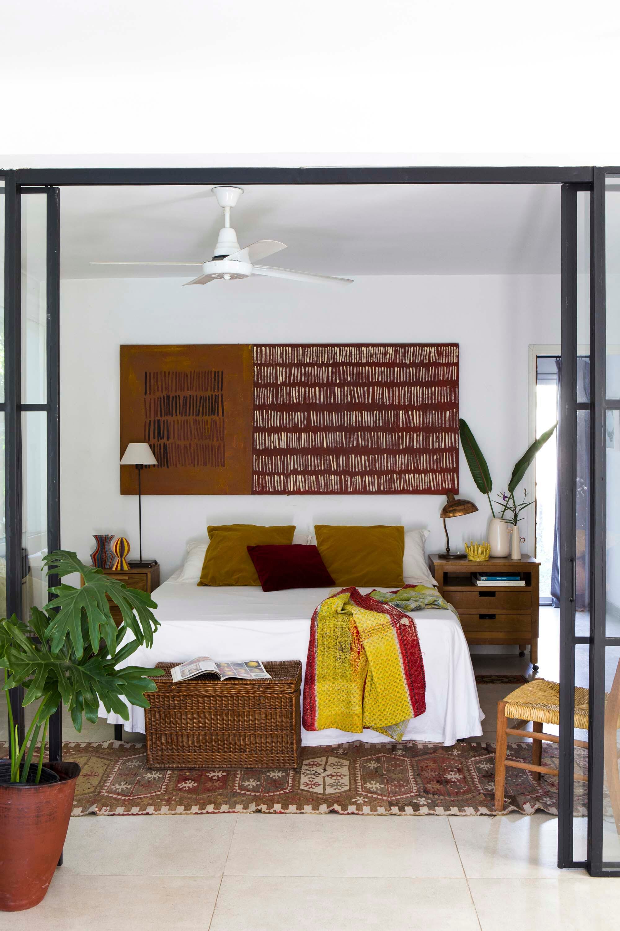 Puerta corrediza en hierro negro y vidrio, que separa el dormitorio de la sala sin perder luz. Sobre el respaldo, una obra que Ángeles pintó en un bastidor de madera que encontró dando vueltas en su taller. La alfombra era de su madre, que la trajo de Turquía hace años.