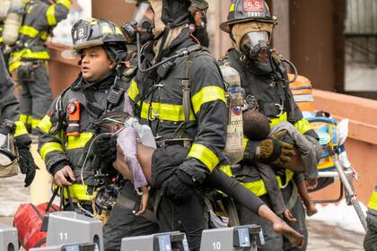 9 de enero de 2022, EE. UU., Nueva York: los bomberos sacan a los niños después de que estallara un incendio dentro de un apartamento dúplex en el tercer piso de un edificio de apartamentos del Bronx, que dejaron al menos 19 muertos, incluidos 9 niños. (New York Daily News)