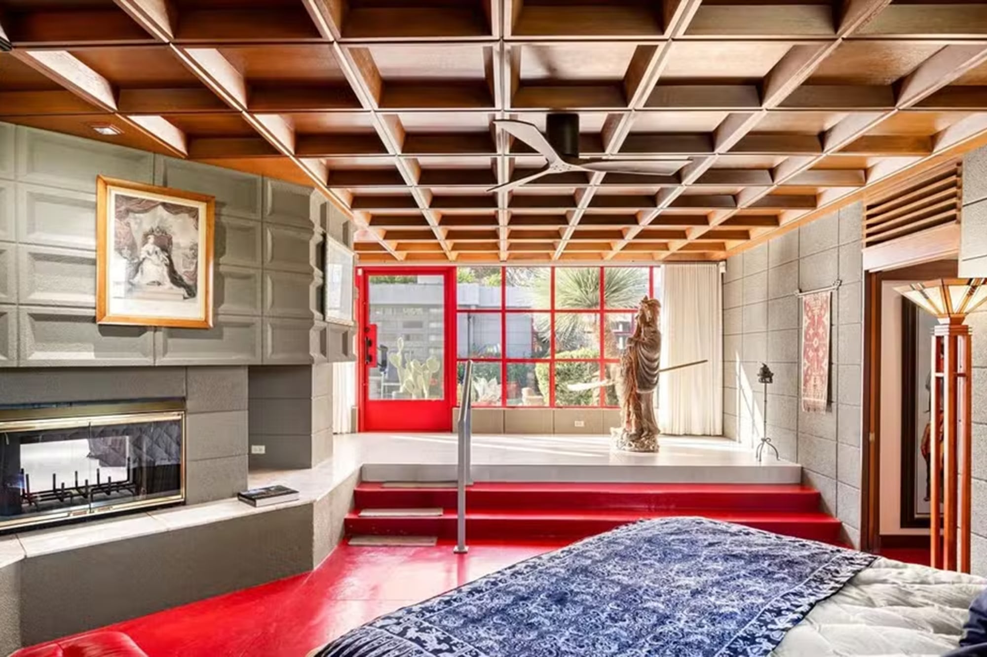 El suelo rojo complementa las ventanas del mismo tono, mientras que la chimenea y la luz natural aportan calidez a esta estancia