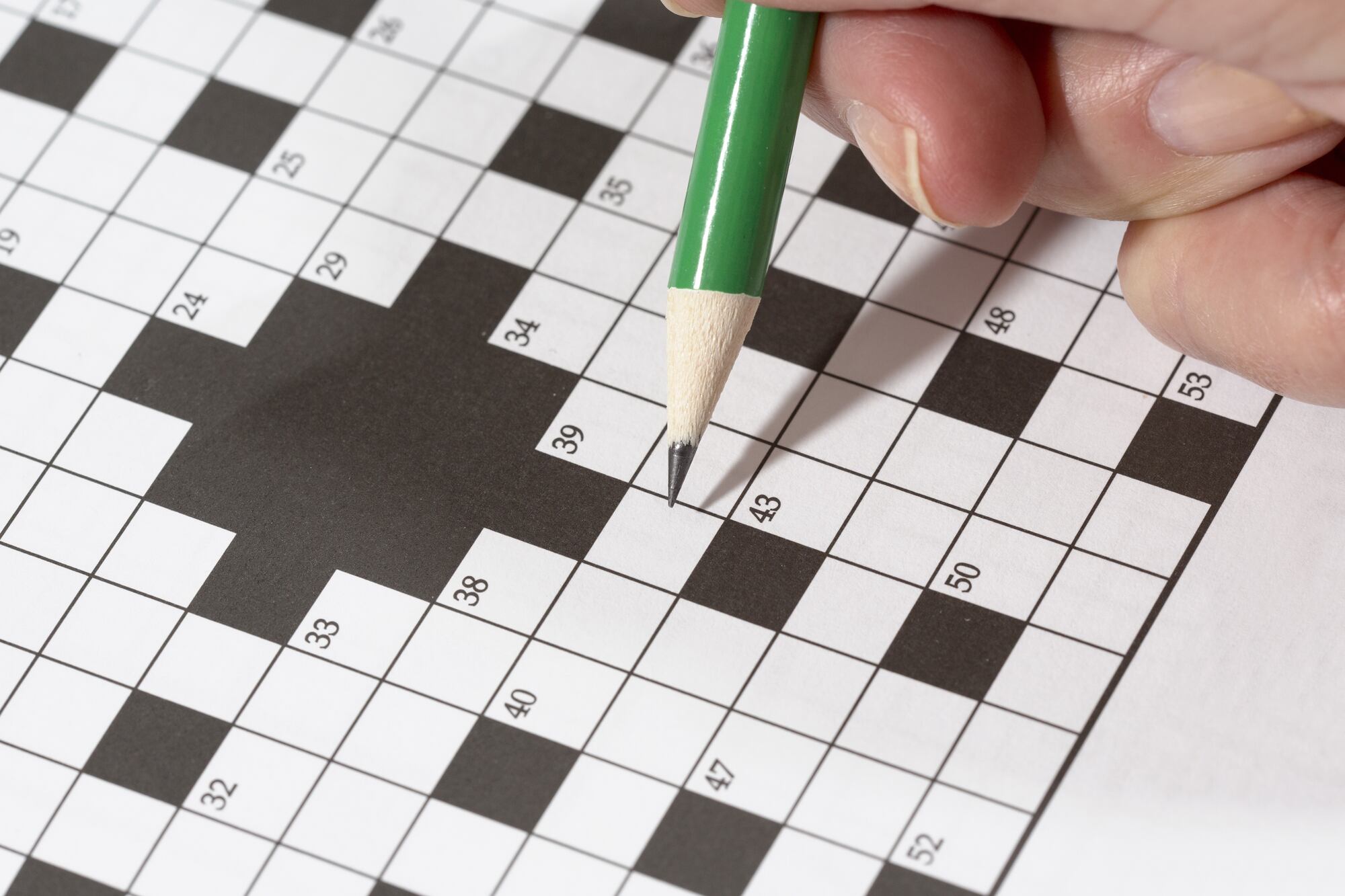 An elderly woman is doing crossword puzzle with a pencil. This is a good exercise for older people to train their brains.