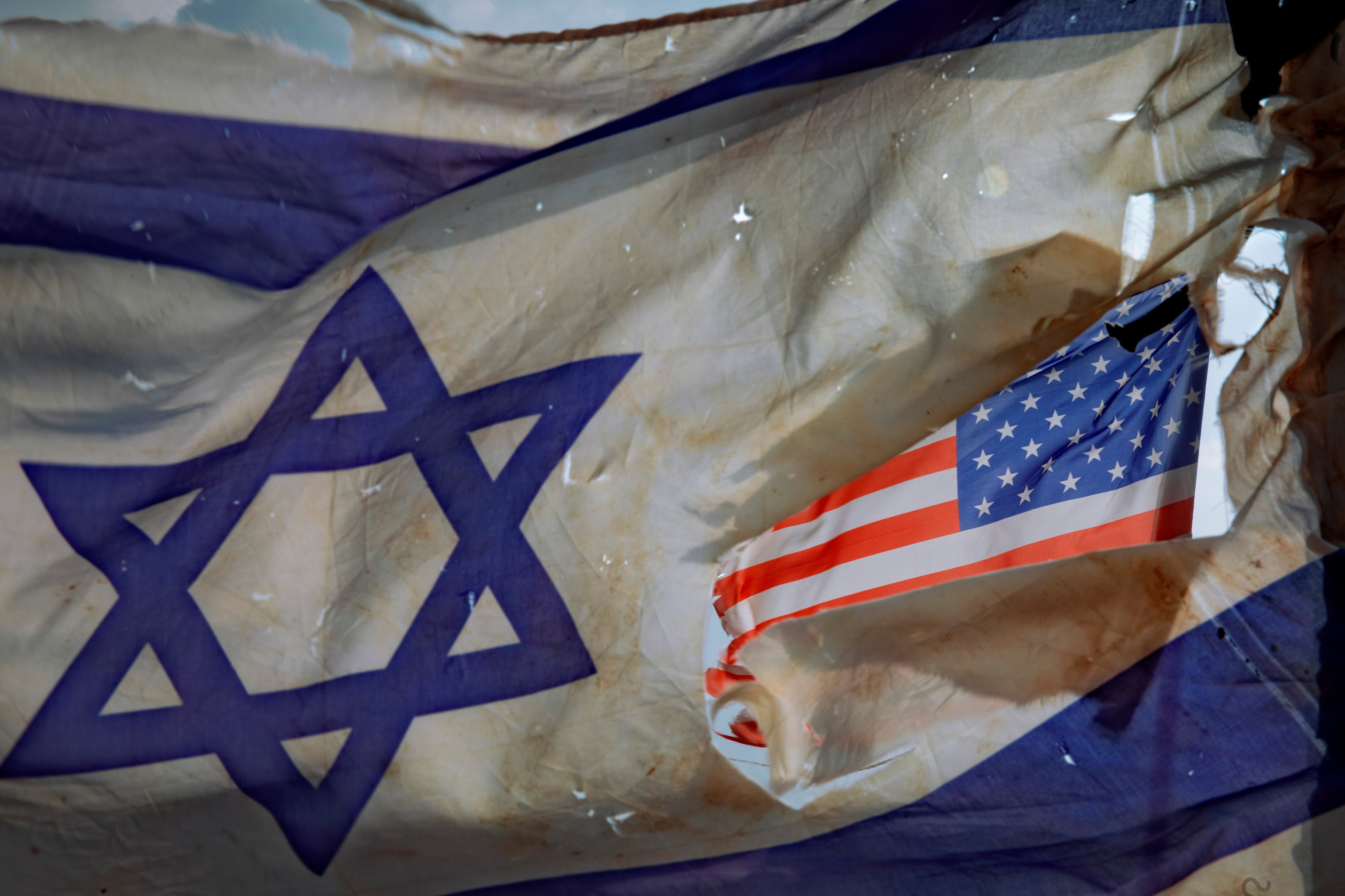 ARCHIVO- Una bandera estadounidense vista a través de un agujero abierto en una bandera nacional de Israel mientras ambas ondean en el viento en un criadero de caballos, cerca de la ciudad de Sderot, en el sur de Israel, el viernes 20 de noviembre de 2020. (AP Foto/Oded Balilty, Archivo)