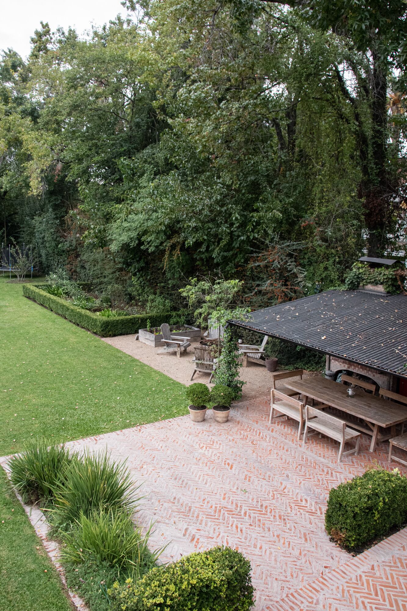 Desde la pérgola del quincho, se ve un diseño de huerta y fogón, a la sombra de Bauhinia forficata del vecino, y repitiendo la especie de este lado.