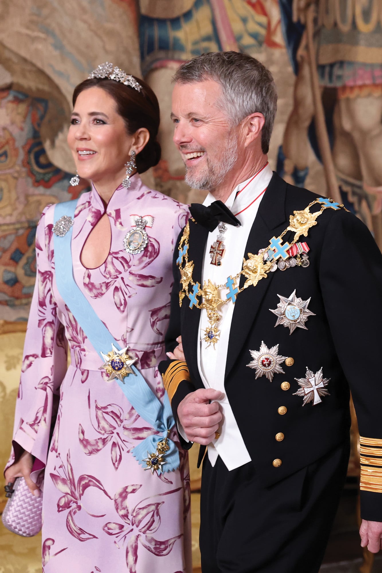 Los reyes Federico X y Mary de Dinamarca, sonrientes y de la mano. Para la gala, ella estrenó un vestido de inspiración oriental de Soeren Le Schmidt, confeccionado en un tejido rosa con reflejos malva, y lo acompañó con clutch Bottega Veneta y las alhajas más especiales: la pulsera reconvertida en gargantilla que también puede usarse como tiara