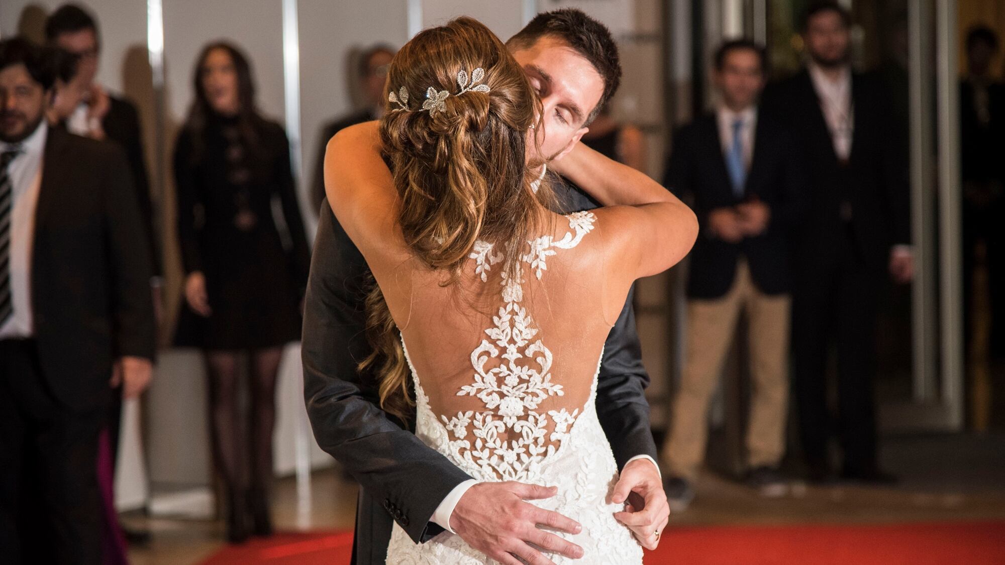 La espalda del vestido tenía forma de corazón con apliques en guipur blancos; la novia llevó el cabello en un semi recogido con ondas y un aplique de flores plateadas