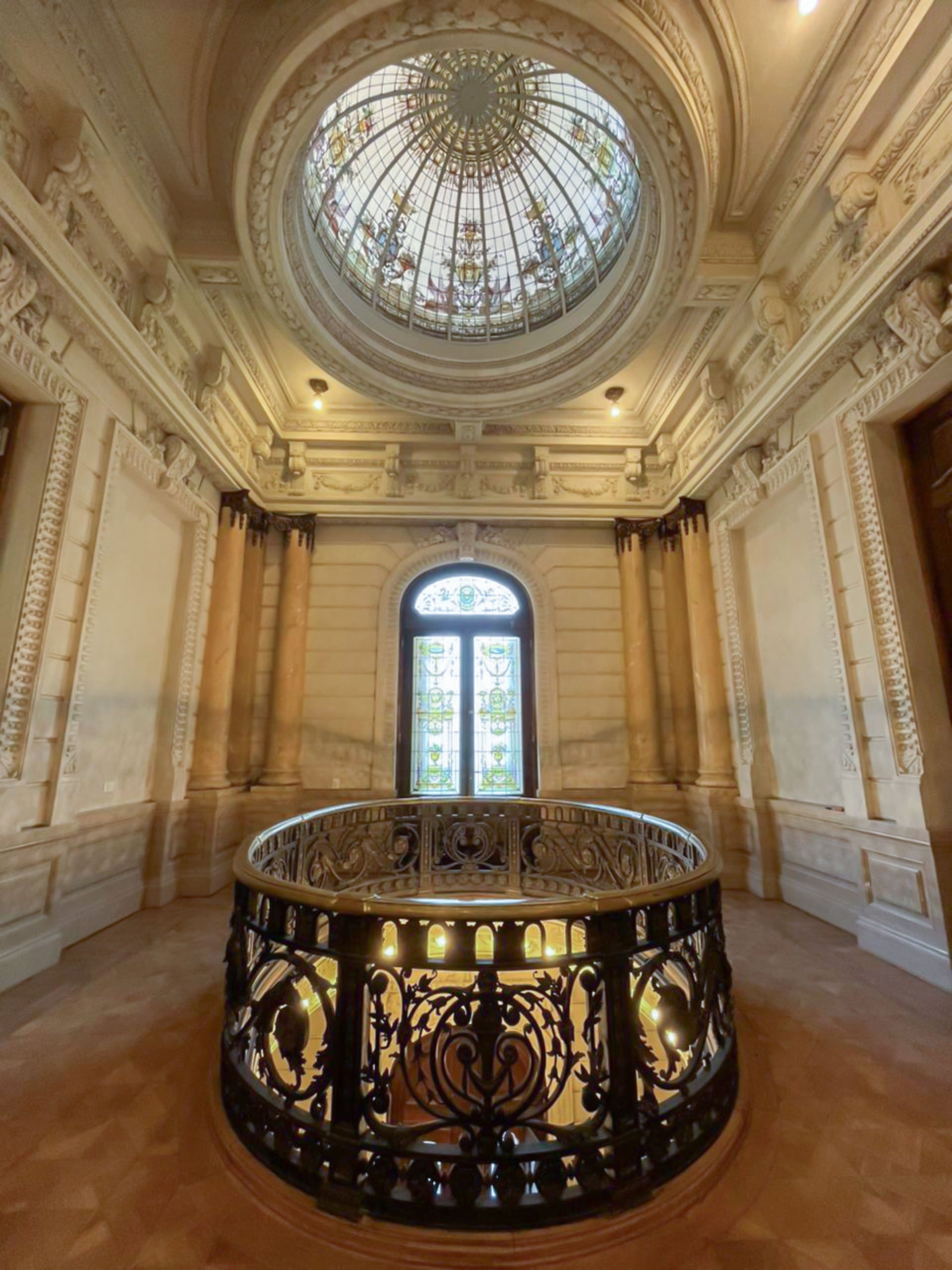 El Vitral Cenital: Lo más llamativo es la cúpula con un vitral circular que permite la entrada de luz natural, decorado con motivos heráldicos y florales clásicos de la época.