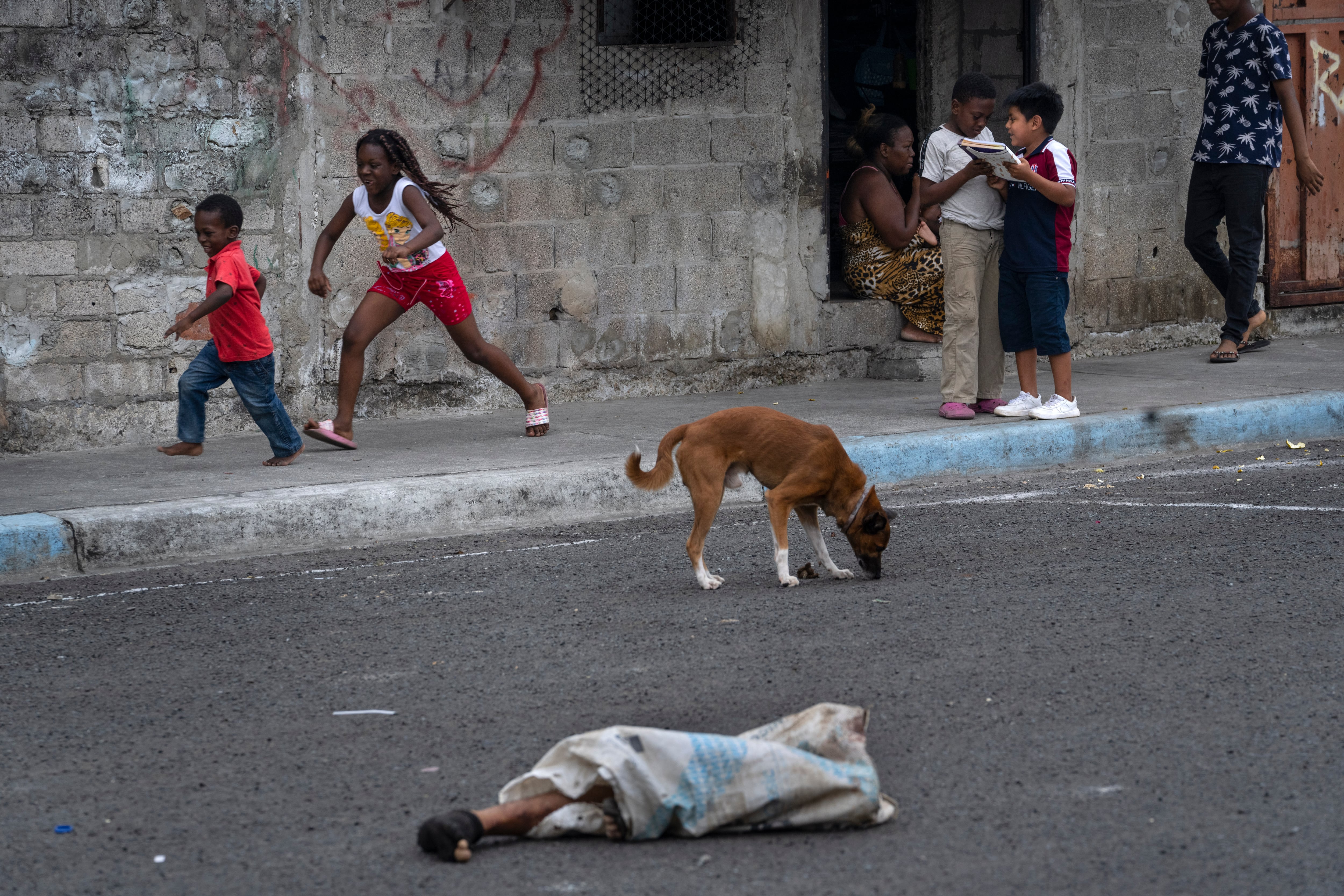 Las piernas de un hombre desmembrado sobresalen de una bolsa en la calle donde juegan niños y deambulan perros en el barrio Colinas de La Florida en Guayaquil, Ecuado (Foto AP/Rodrigo Abd)