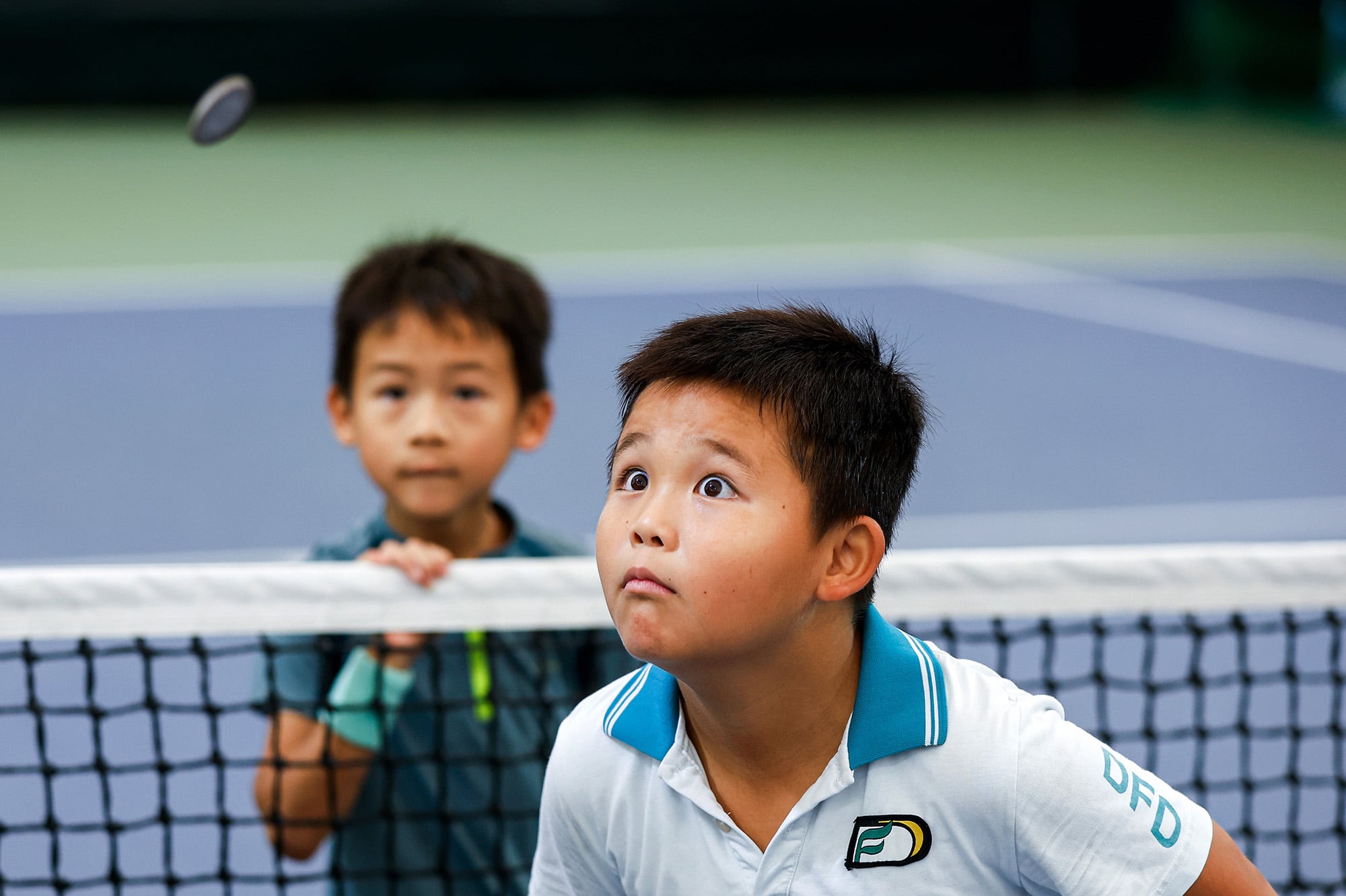La fotografía que logró el tercer lugar, tomada durante la final de un torneo local de tenis junior en Guangzhou, China, muestra un lanzamiento de moneda entre dos jóvenes jugadores, quienes observan atentamente la moneda en el aire