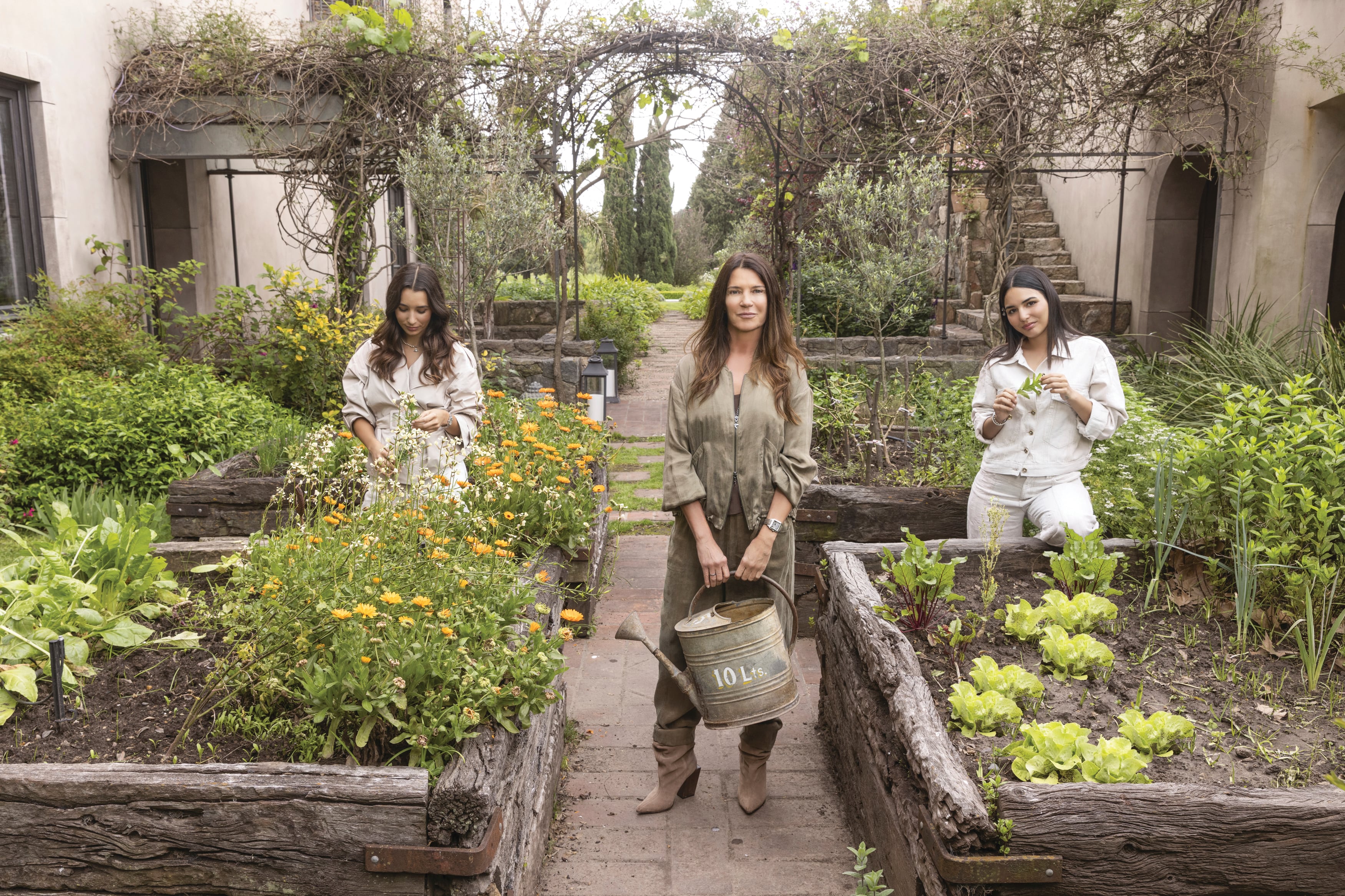 La madre y sus hijas posan para ¡HOLA! Argentina en la huerta. A la izquierda: Victoria, con un trench cruzado y pantalón de lino
wide leg; en el centro, Gabriela, con un conjunto de campera con doble cierre y pantalón, ambos confeccionados con un textil satinado con efecto durazno; y a la derecha, Paula, con campera y pantalón wide leg
realizados con un tejido de Jacquard y algodón oversized