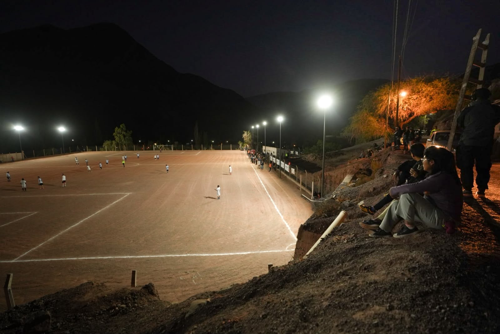 Un grupo de personas se reúne en el cerro para ver el partido que ocurrió poco después de la inauguración de la red de iluminación en la cancha