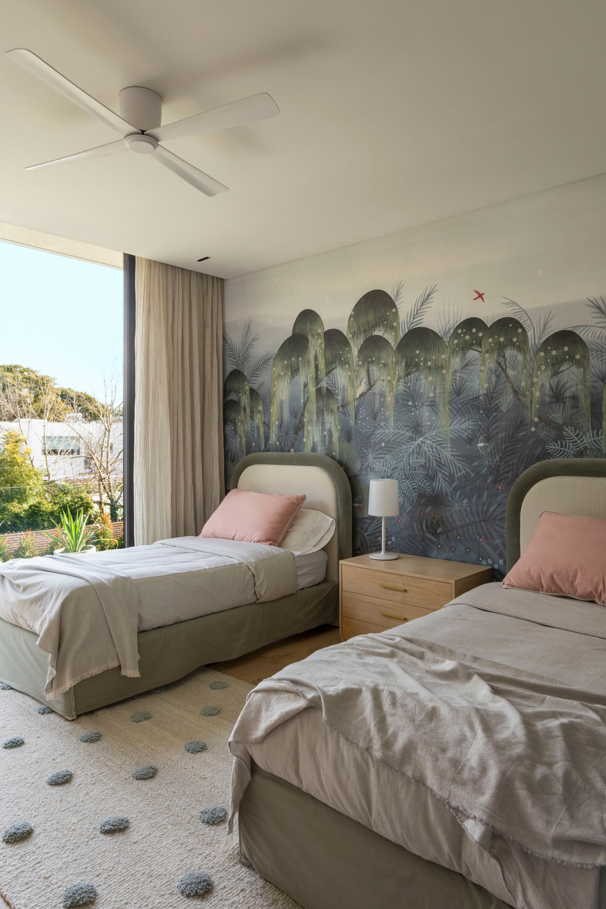 El cuarto de las hijas, revestido con el mural ‘Bosque de los Magos’ (Mercedes Costal), tiene camas con respaldo entelado (Melazza) y alfombra ‘Pompones’ (Elementos Argentinos).