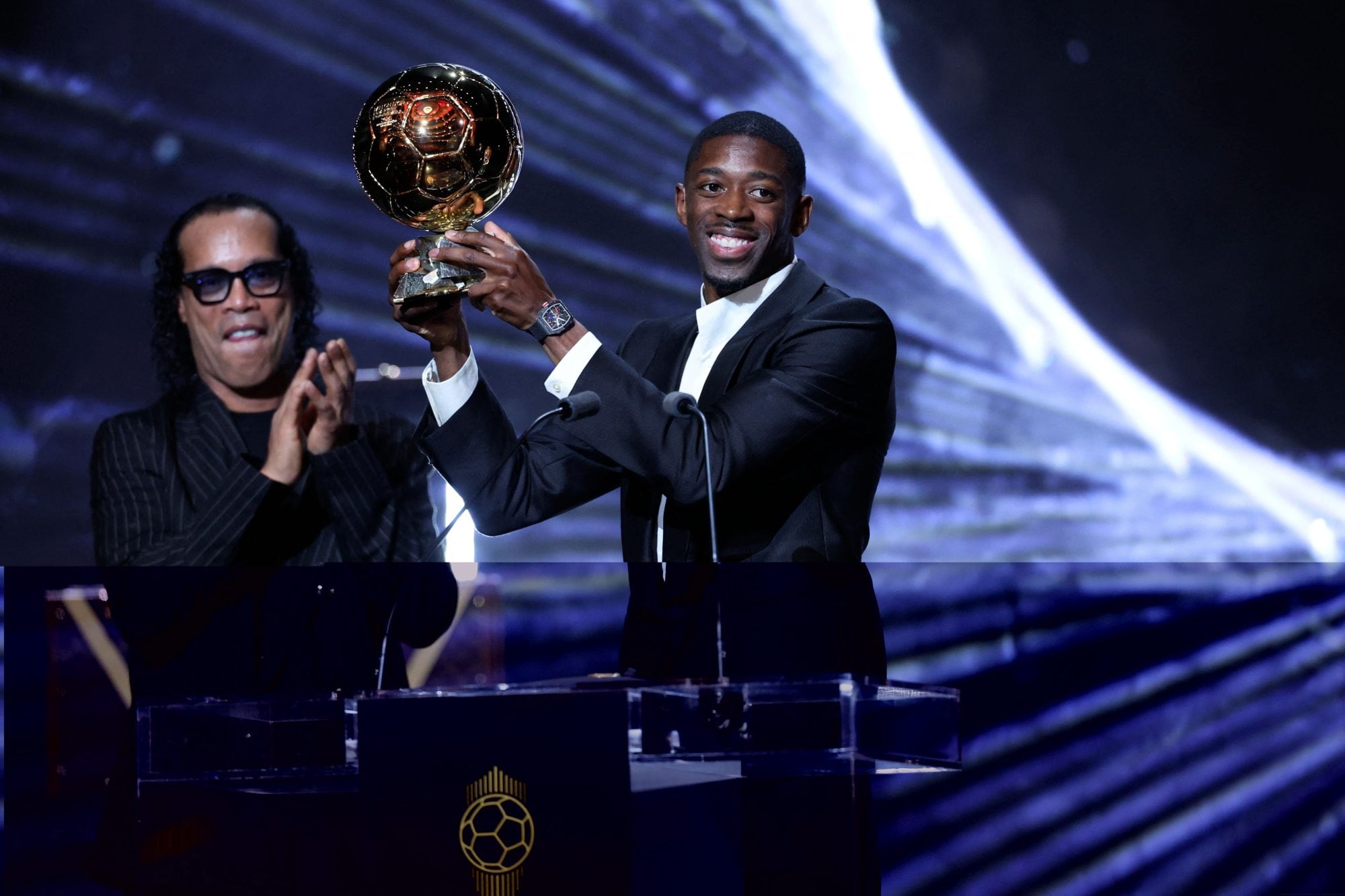 Ousmane Dembele, con el balón de oro entre sus manos; detrás, Ronaldinho