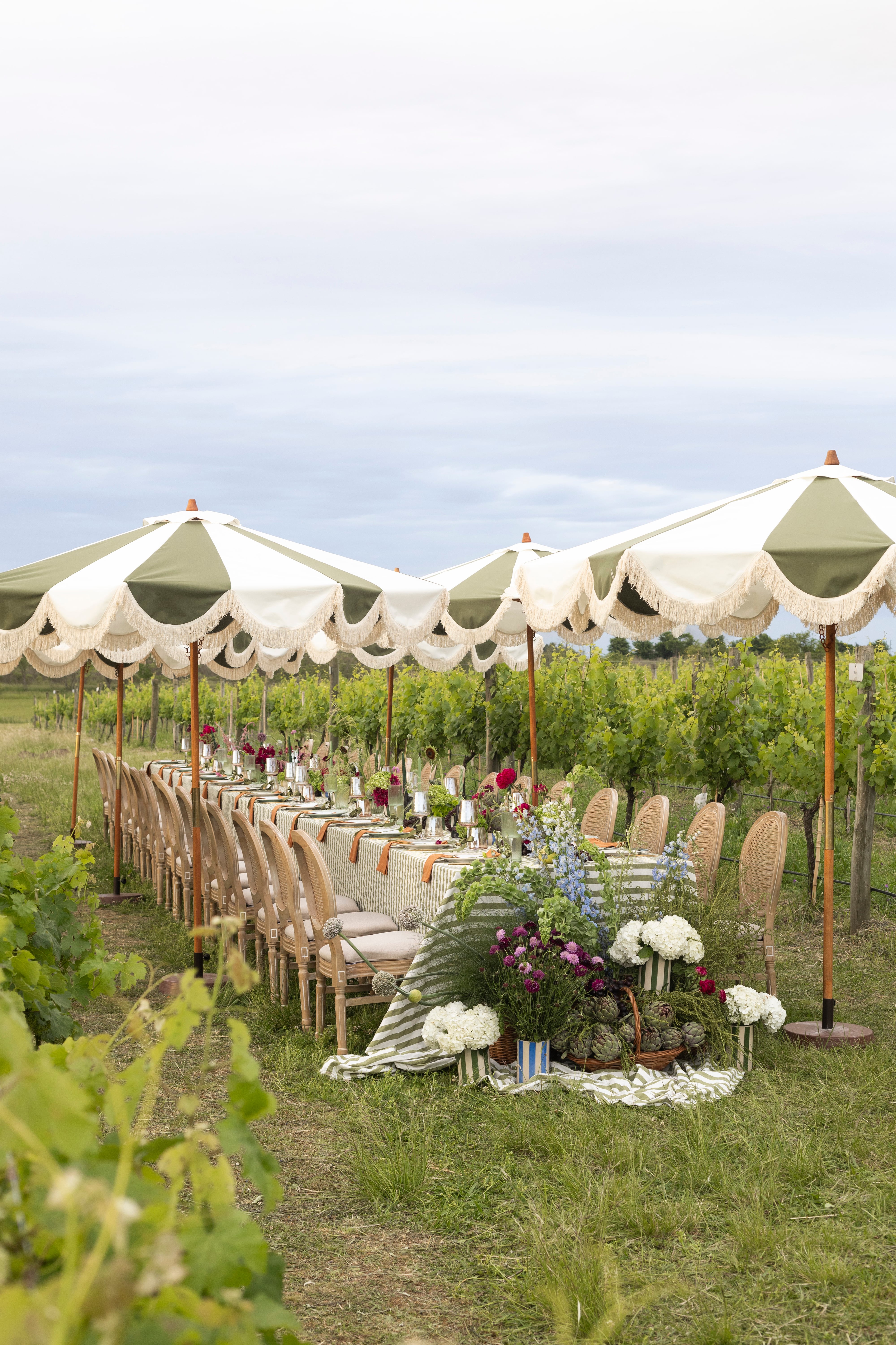 Una mesa que se funde con el paisaje del viñedo: textiles en tonos verdes y detalles naturales que dialogan con el entorno para crear una experiencia única al aire libre.