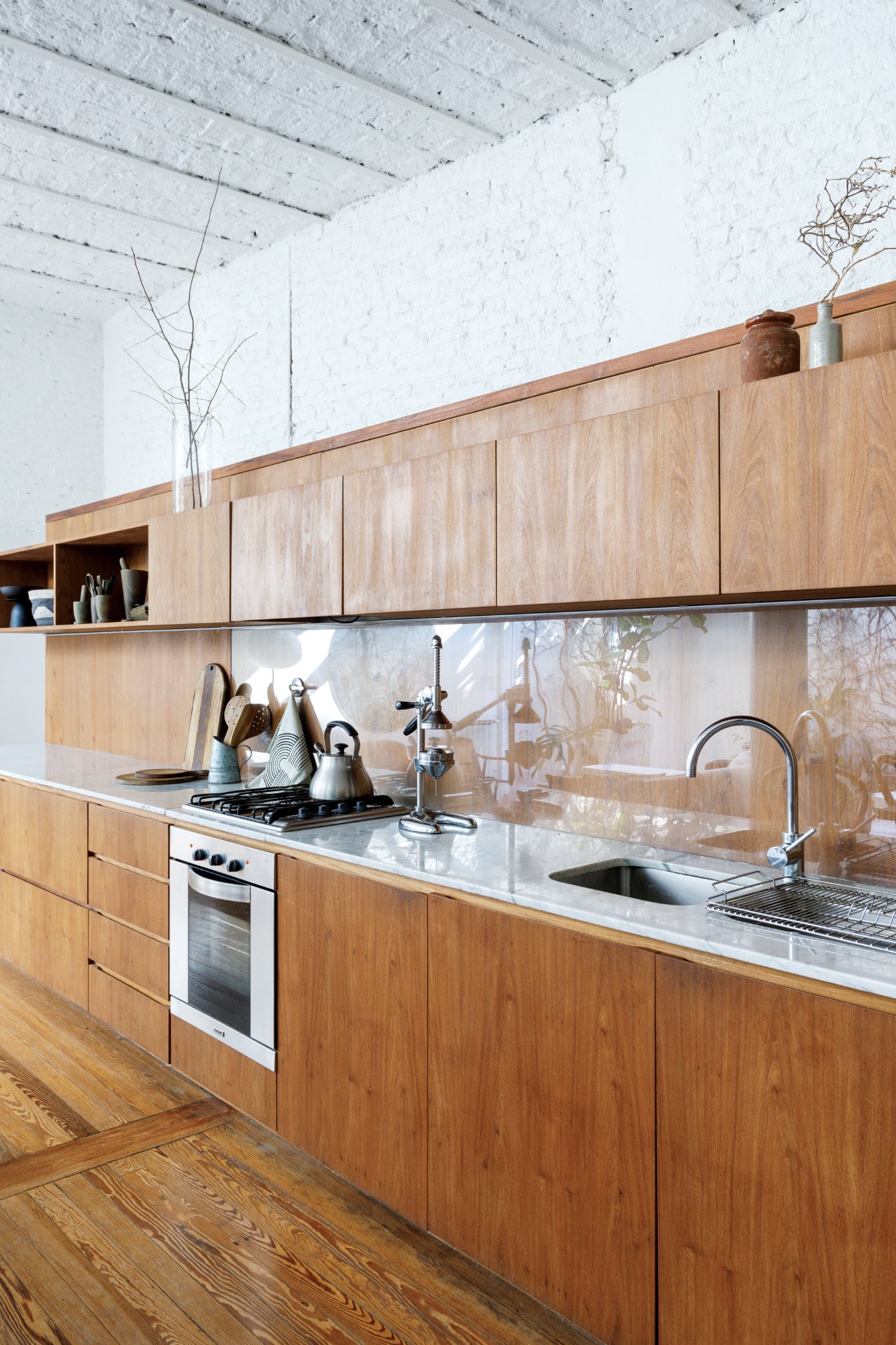 En esta cocina con tanta presencia de la madera, la mitad de la alzada se cubrió con vidrio, para protegerla y facilitar la limpieza.
