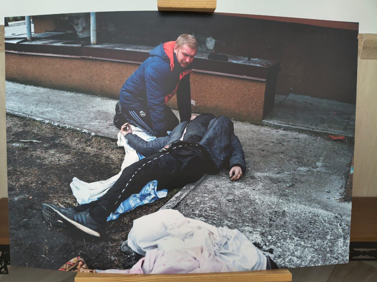 La fotografía de la exposición muestra un civil cargando a un cadáver por las calles de Bucha, Ucrania