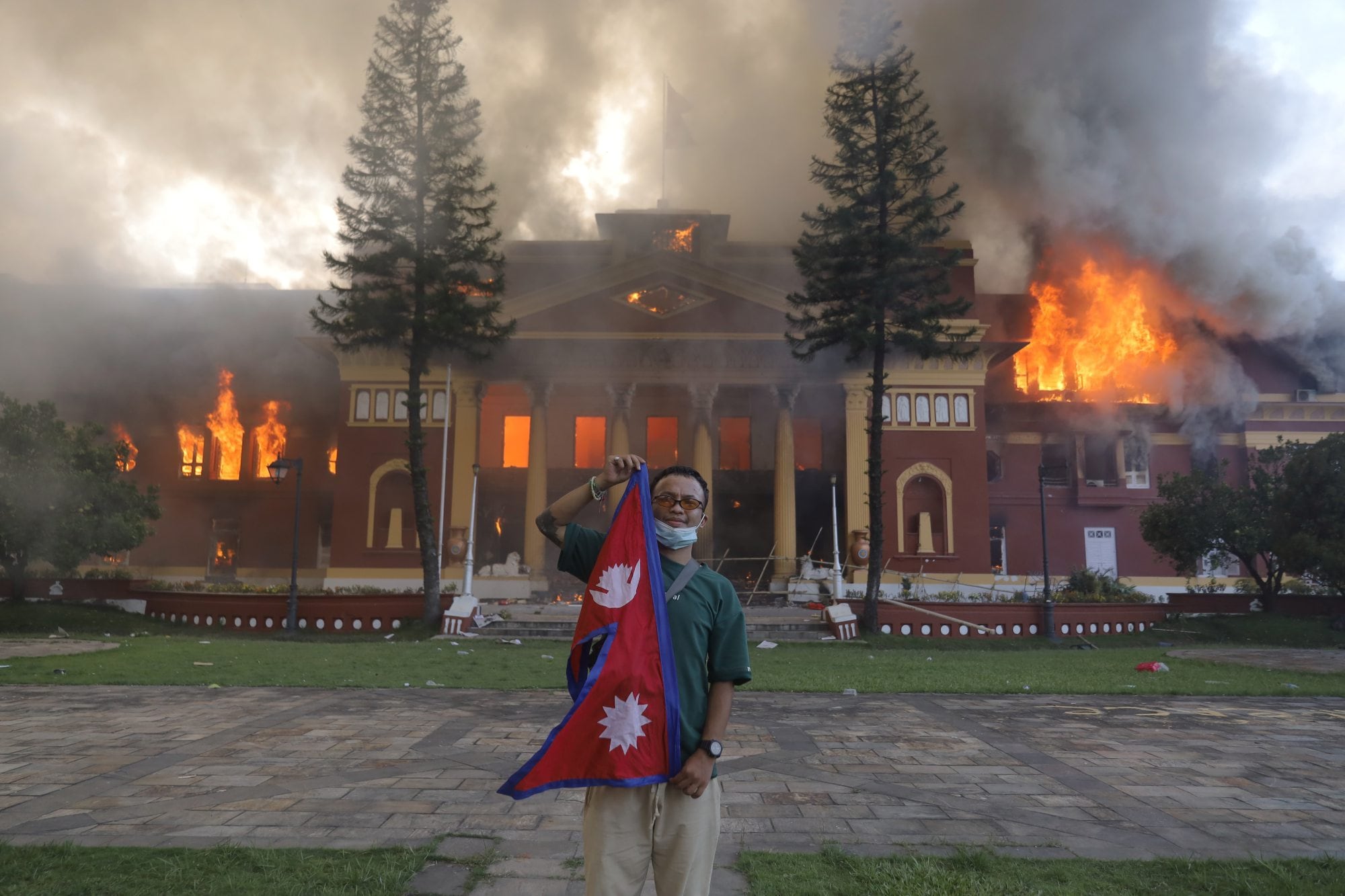 Un manifestante posa frente al palacio presidencial en Katmandú mientras el edificio arde durante las protestas del 9 de septiembre de 2025