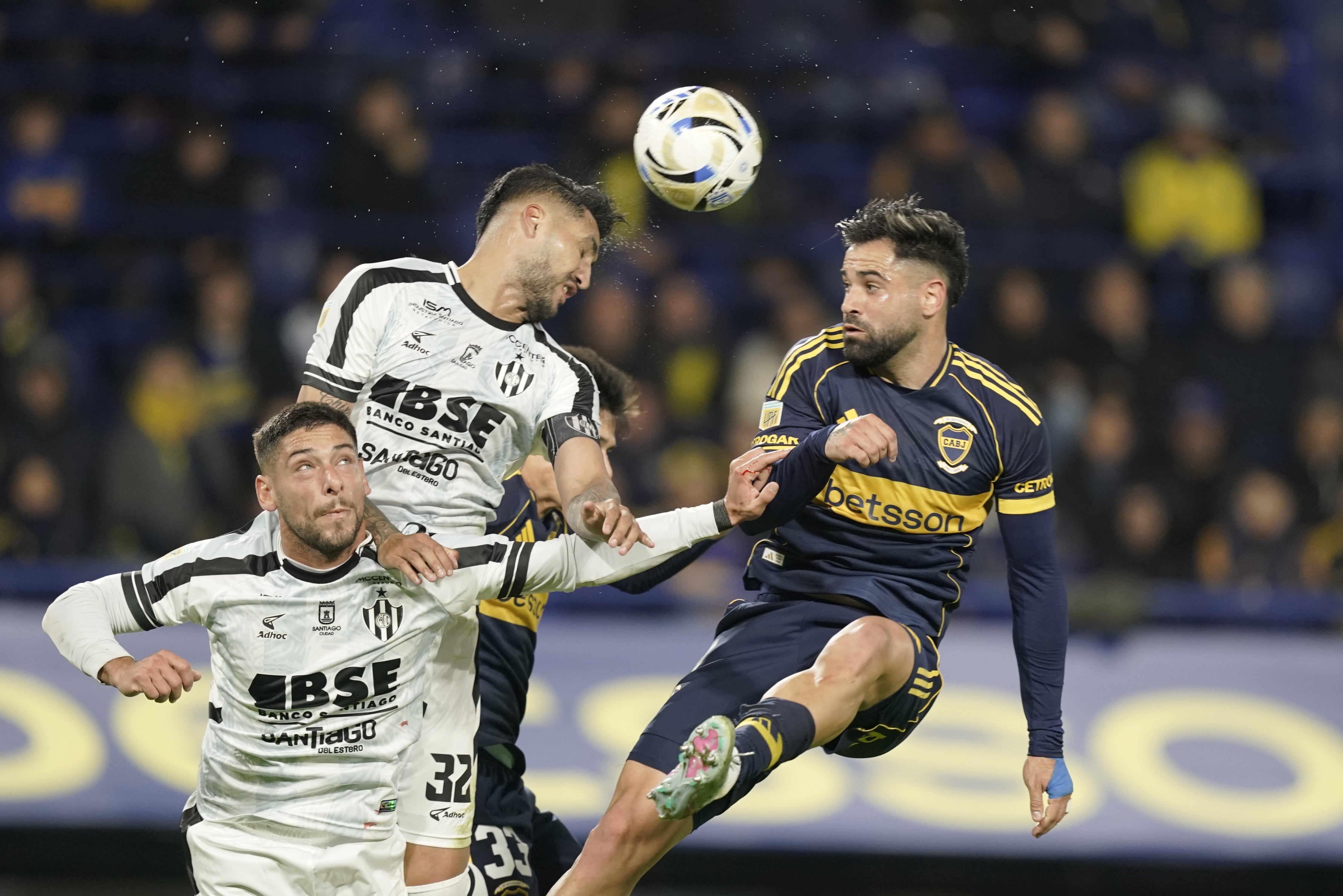 Lucha en lo alto por la pelota entre Jonathan Galván y Milton Giménez; más abajo no llega Lucas Abascia