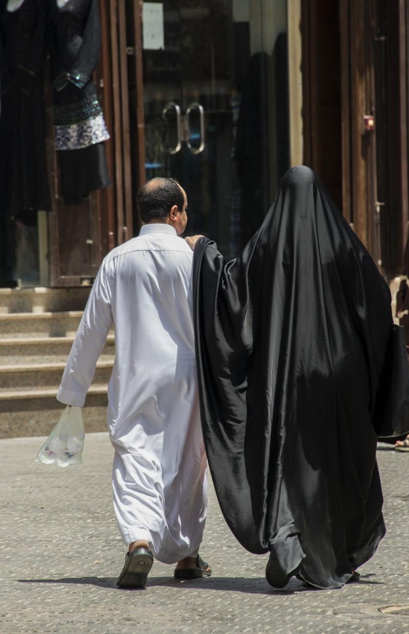 Una pareja saudita camina por las calles de Al Balad, vestidos con la vestimenta tradicional