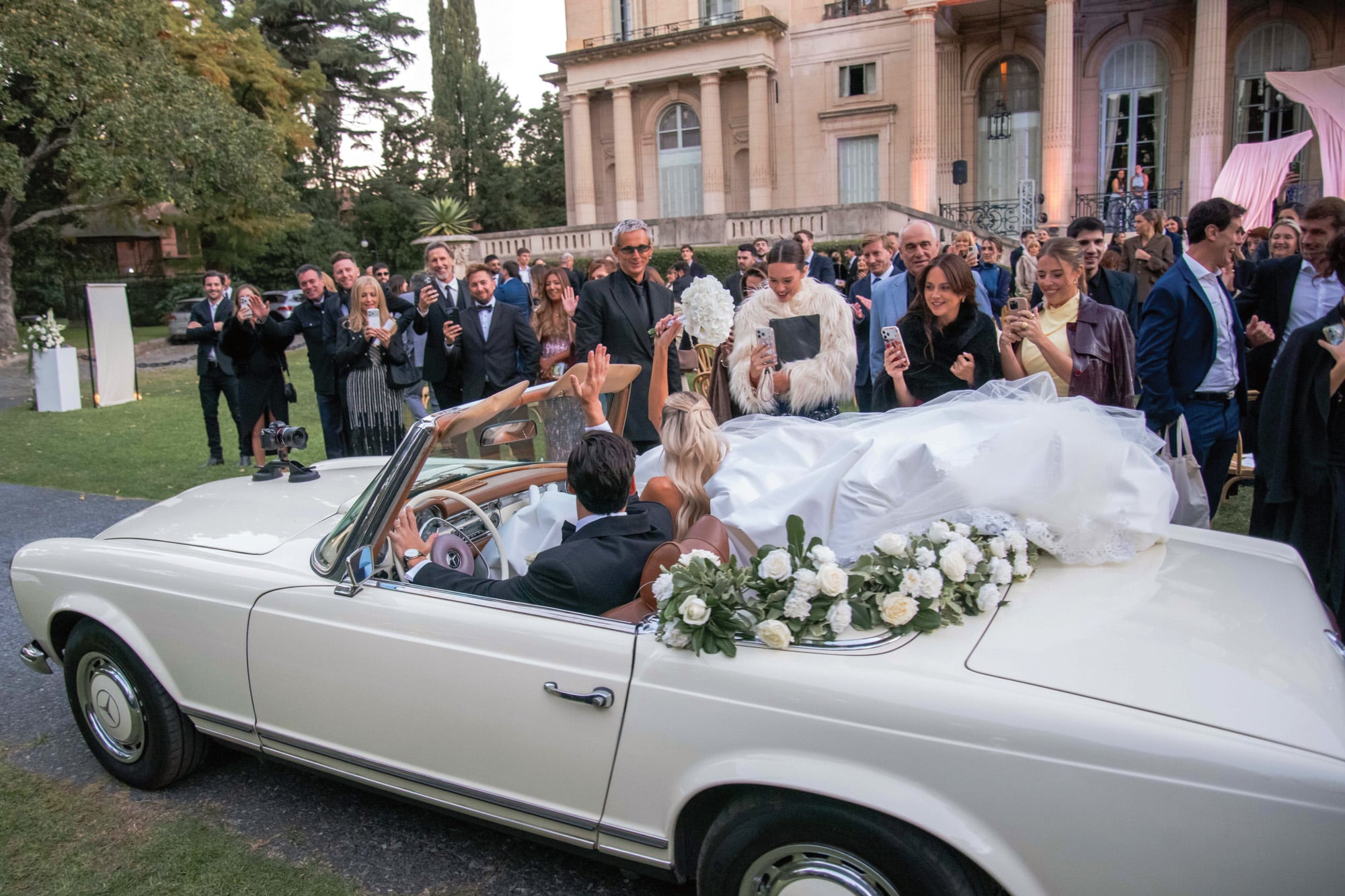 Tras la ceremonia, los novios saludan a los invitados desde un
Mercedes-Benz modelo 280 SL de 1969. En primera fila, las
amigas de la novia Manuela Viale (con un tapado blanco) y
Nati Jota (lookeada con vestido amarillo y chaqueta de cuero)
congelan el momento con su celular