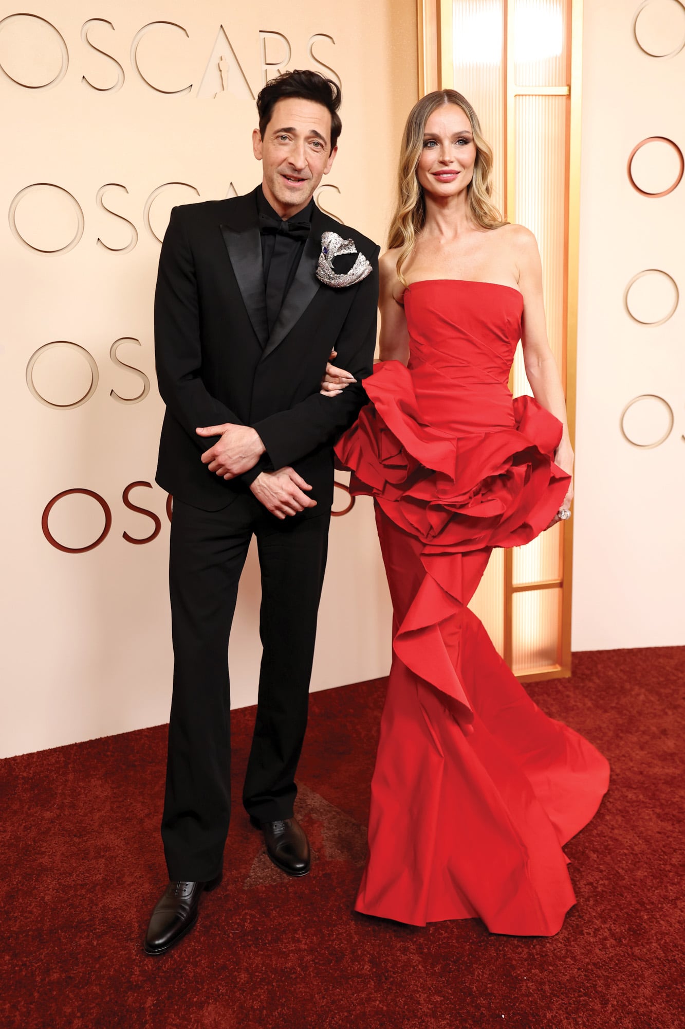 Adrien Brody con smoking negro con solapas de seda. Su novia, la diseñadora Georgina Chapman, lució un fabuloso vestido rojo con volantes en 3D