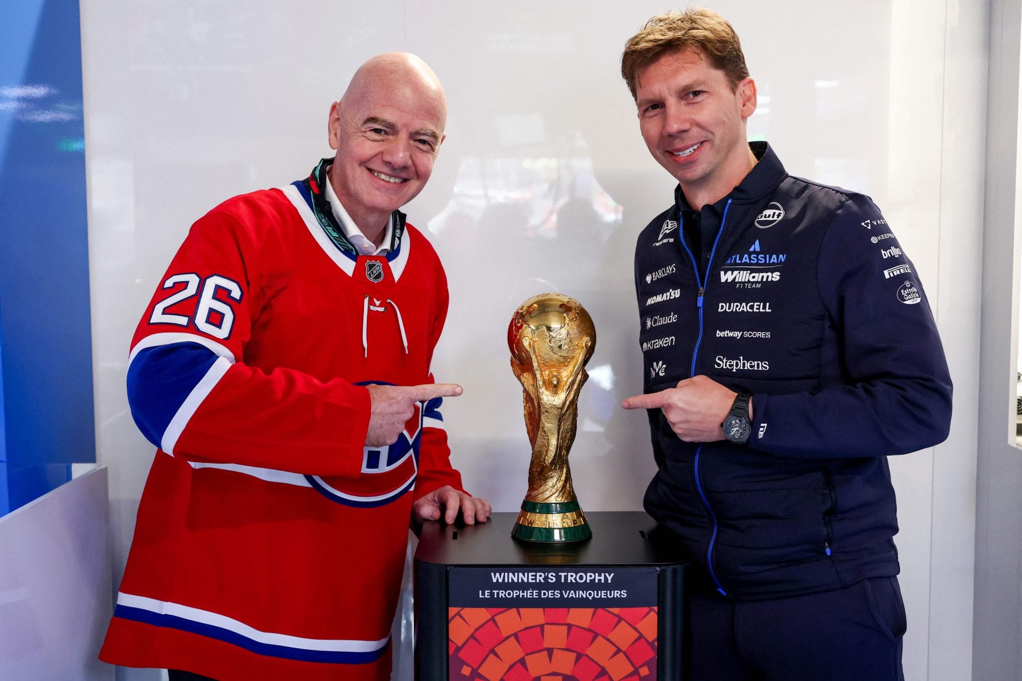 Gianni Infantino, presidente de la FIFA, junto a James Vowles, director de Williams; juntos posan con el trofeo dle Mundial, que tendrá a Canadá como una de sus tres sedes